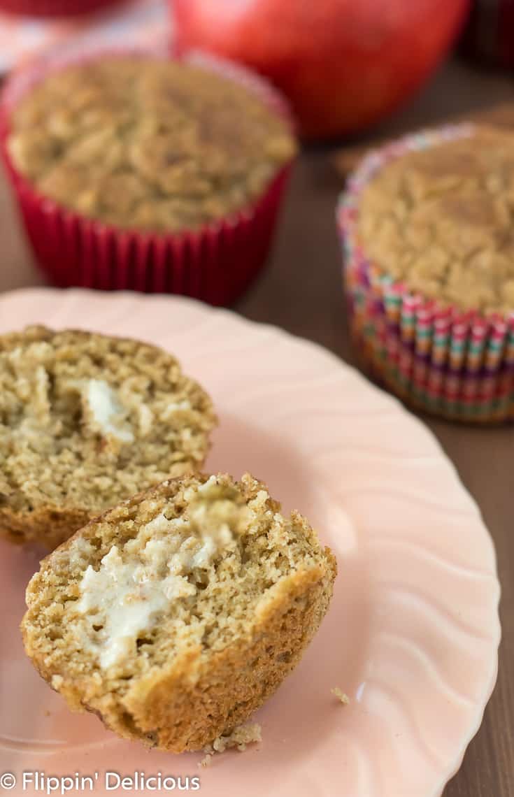 a gluten free apple cinnamon muffin cut in half and spread with butter, sitting on a peach plate with more gluten free muffins in the background