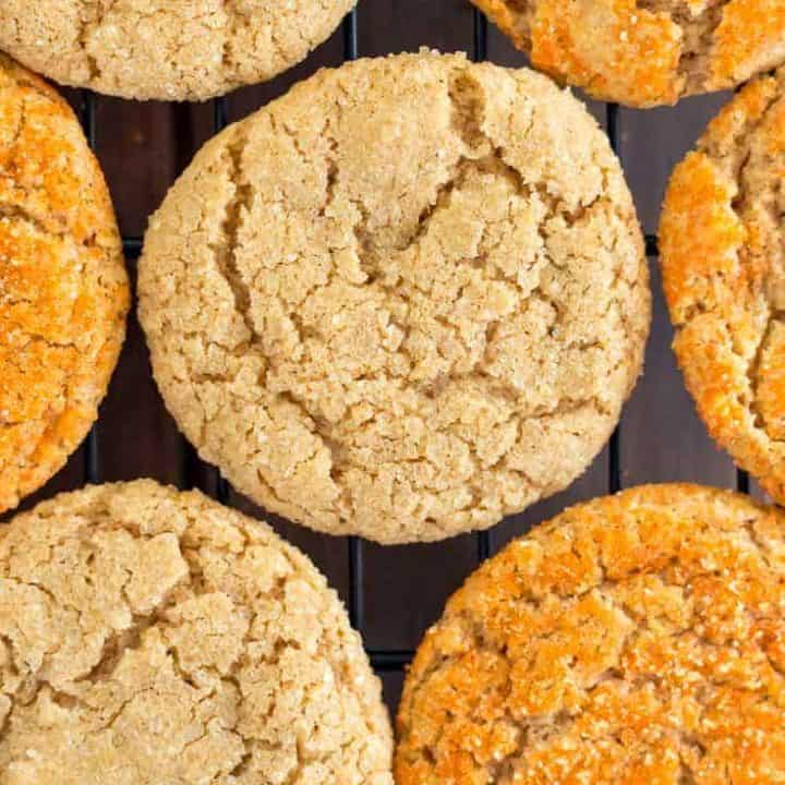 Overhead photo of vegan gluten free pumpkin sugar cookies on a black cooling rack, half sprinkled with orange sanding sugar and half with coarse raw sugar