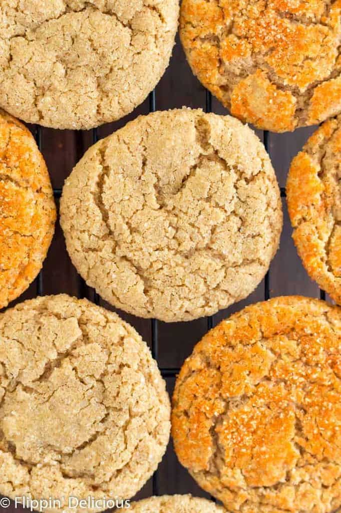 Overhead photo of vegan gluten free pumpkin sugar cookies on a black cooling rack, half sprinkled with orange sanding sugar and half with coarse raw sugar