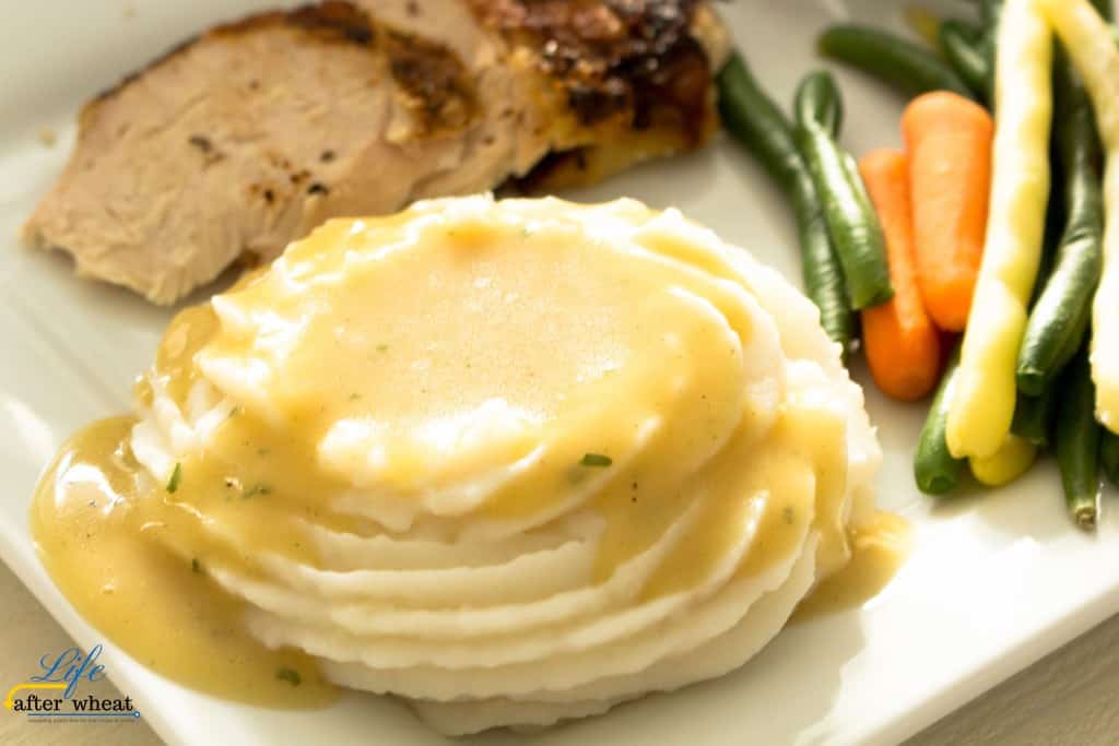 gluten free gravy over mashed potatoes with green beans, carrots,and turkey in the background