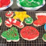 gluten free sugar cookie cutouts shaped like holiday tree, cane, stocking, and star on a cooling rack, topped with green, red, yellow, and white frosting and holiday sprinkles