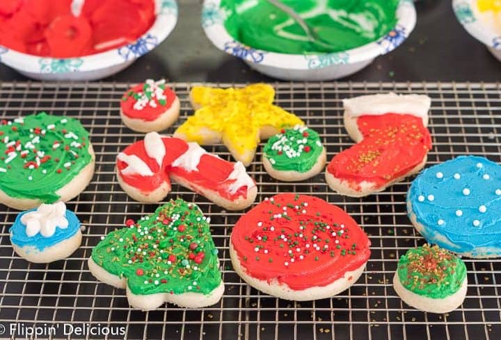 gluten free sugar cookie cutouts shaped like holiday tree, cane, stocking, and star on a cooling rack, topped with green, red, yellow, and white frosting and holiday sprinkles