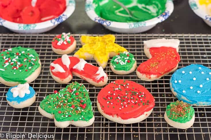 gluten free sugar cookie cutouts shaped like holiday tree, cane, stocking, and star on a cooling rack, topped with green, red, yellow, and white frosting and holiday sprinkles