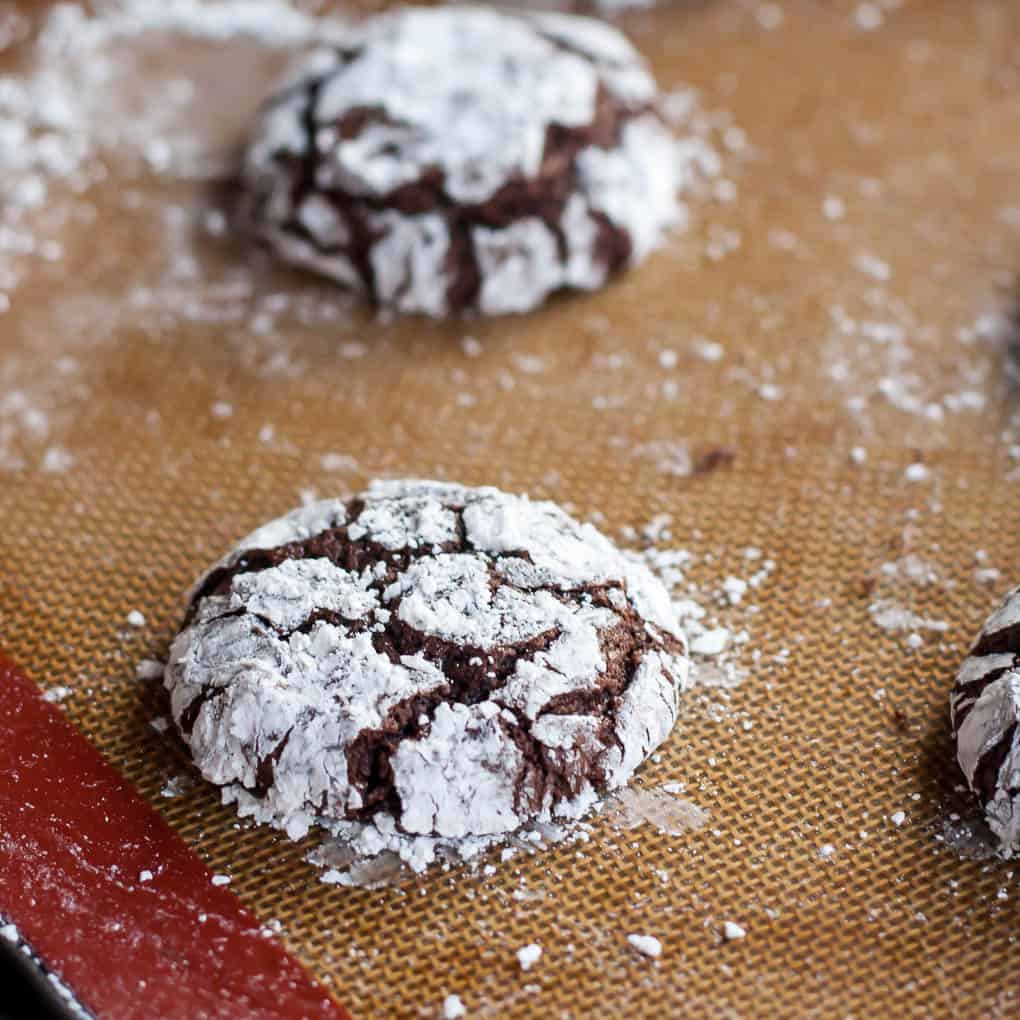 gluten free chocolate crinkle cookies covered in powdered sugar on a silicone baking mat