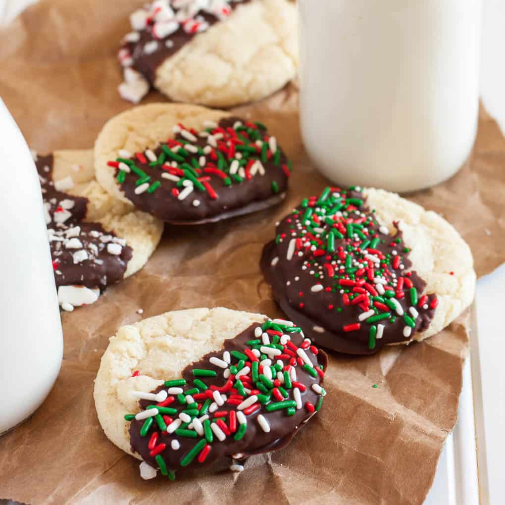 gluten free sugar cookies dipped in chocolate and holiday sprinkles next to glass of milk