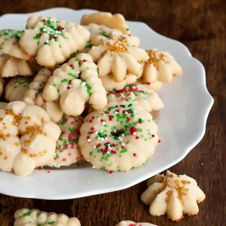 gluten free spritz cookies with red, green, white, and gold sprinkles for the holidays on a white plate