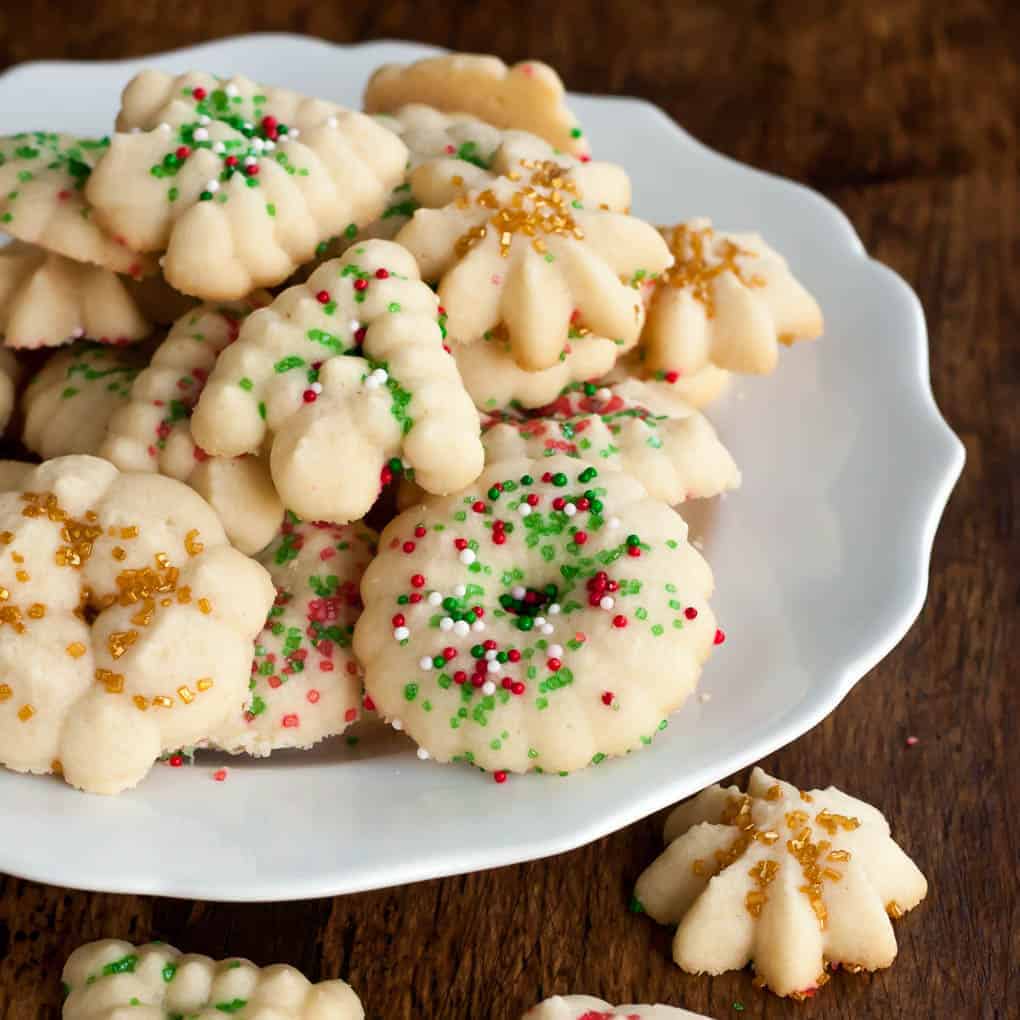 gluten free spritz cookies with red, green, white, and gold sprinkles for the holidays on a white plate 