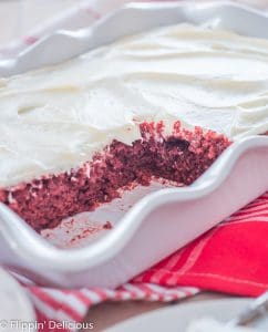scallop-edge white ceramic pan with gluten free red velvet cake with white frosting, with several slices removed