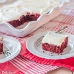 slice of dairy free gluten free red velvet sheet cake topped with white frosting on a white plate with a bite on a small fork with white scallop-edged pan of cake int he background
