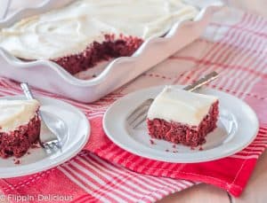 slice of dairy free gluten free red velvet sheet cake topped with white frosting on a white plate with a bite on a small fork with white scallop-edged pan of cake int he background