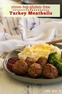 green plate with five gluten free turkey meatballs, mashed potatoes, cherry sauce, and broccoli with a fork and white and purple dish towel in the background
