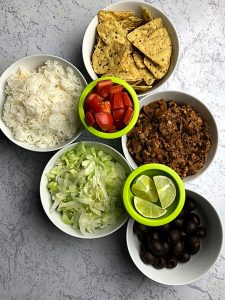overhead view of white bowls filled with ground turkey taco meat, chips, guacamole, tomatoes, and other taco fixings