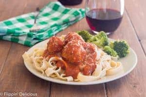 blate full of gluten free pasta and gluten free instant pot turkey meatballs covered in tomatoe sauce with a glass of wine and side of broccoli, with an instant pot in the background