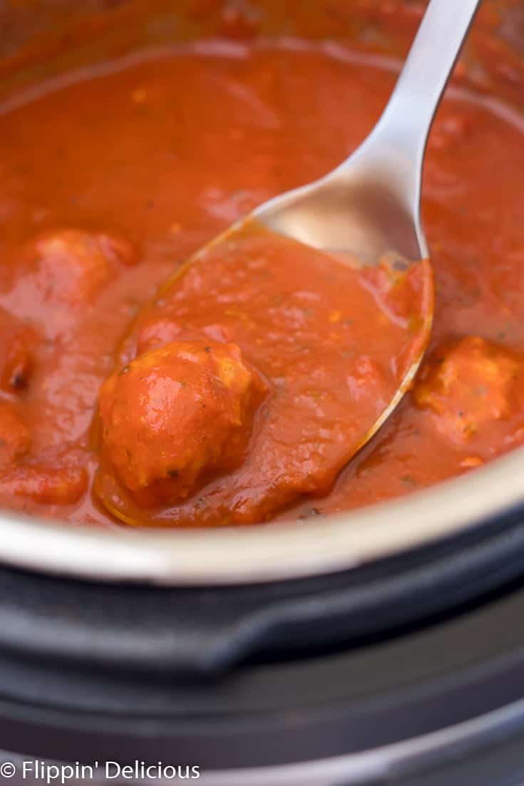 a turkey meatball in a spoonful of tomato sauce being scooped from an Instant Pot pressure cooker