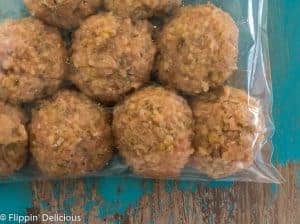 plastic bag full of uncooked gluten free turkey meatballs ready to be frozen, on a teal and grey table.