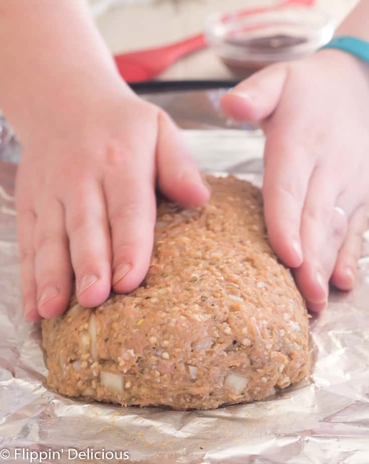 two hands forming a gluten free turkey meatloaf on a baking sheet lined with aluminum foil