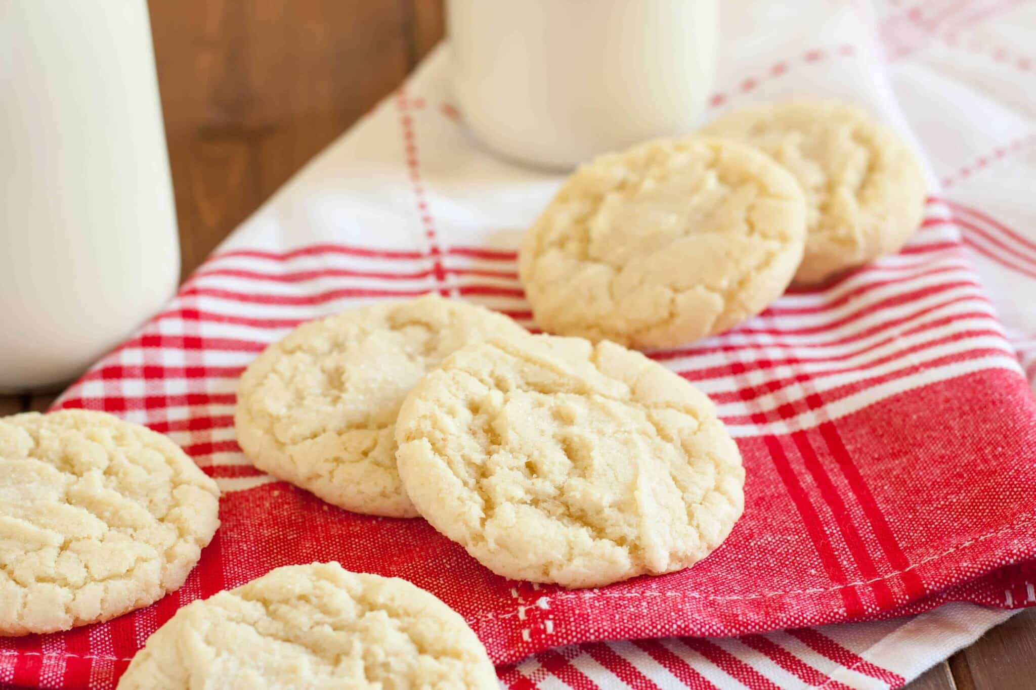 drop gluten free sugar cookies on a red and white striped napkin with a bottle of milk in the background