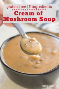 black bowl of gluten free cream of mushroom soup with a spoon full of soup being held just over the bowl with a black and white striped towel in the back with text "gluten-free | 5 ingredients cream of mushroom soup"