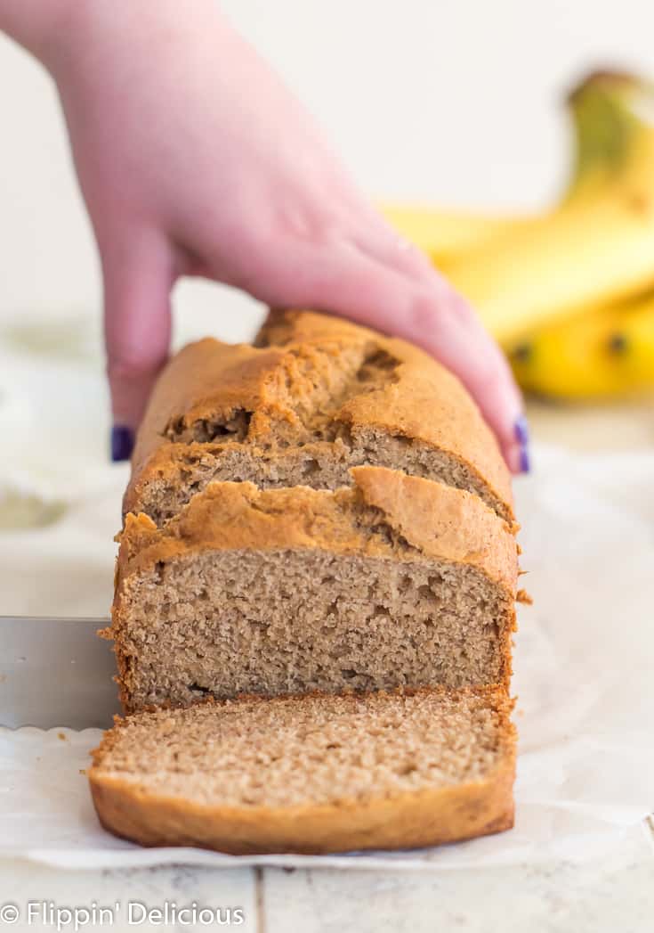 hand holding loaf of gluten free banana bread steady whille cutting with a serrated knife 