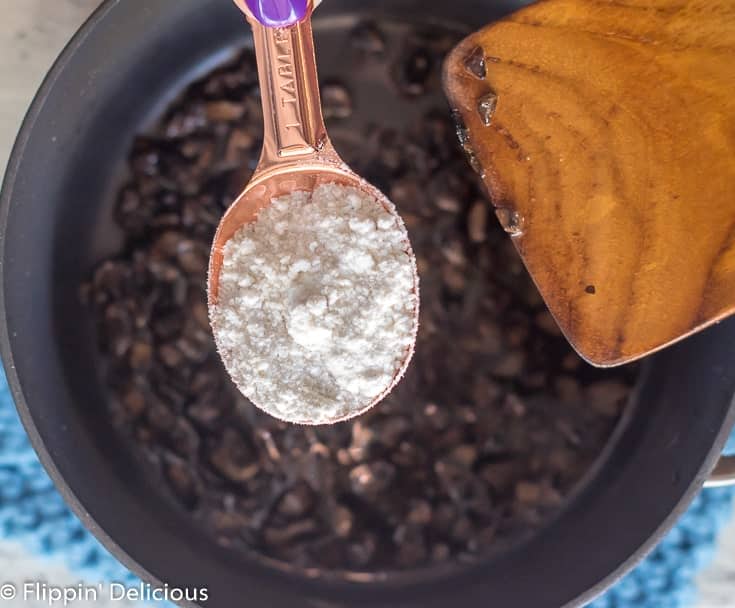 copper spoon adding gluten free flour to sauteed mushrooms in saucepan 