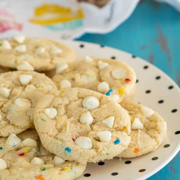 gluten free cookies with white chocolate chips and sprinkles on a cream plate with polka dots on top of a turquoise background with a cupcake dishtowel in the background