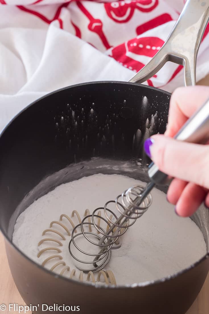 whisking cornstarch and sugar in a saucepan to make gluten free pudding with red and white dishtowel in the back