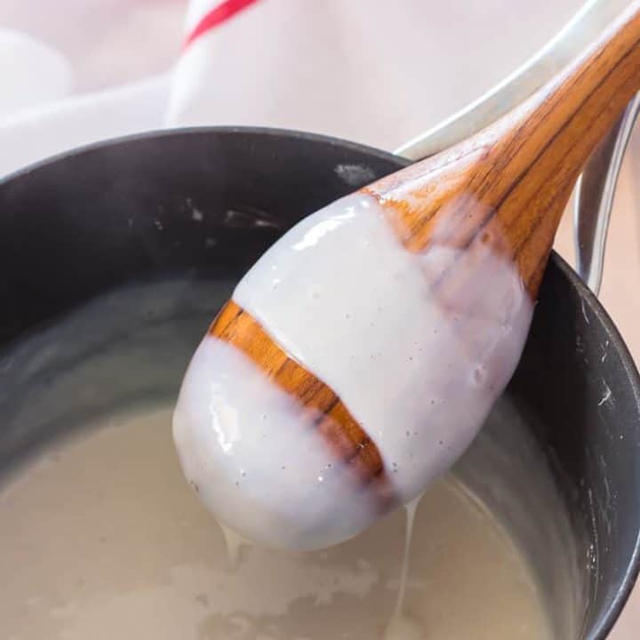 gluten free pudding coating the back of a wooden spoon over a saucepan with dish towel in the back