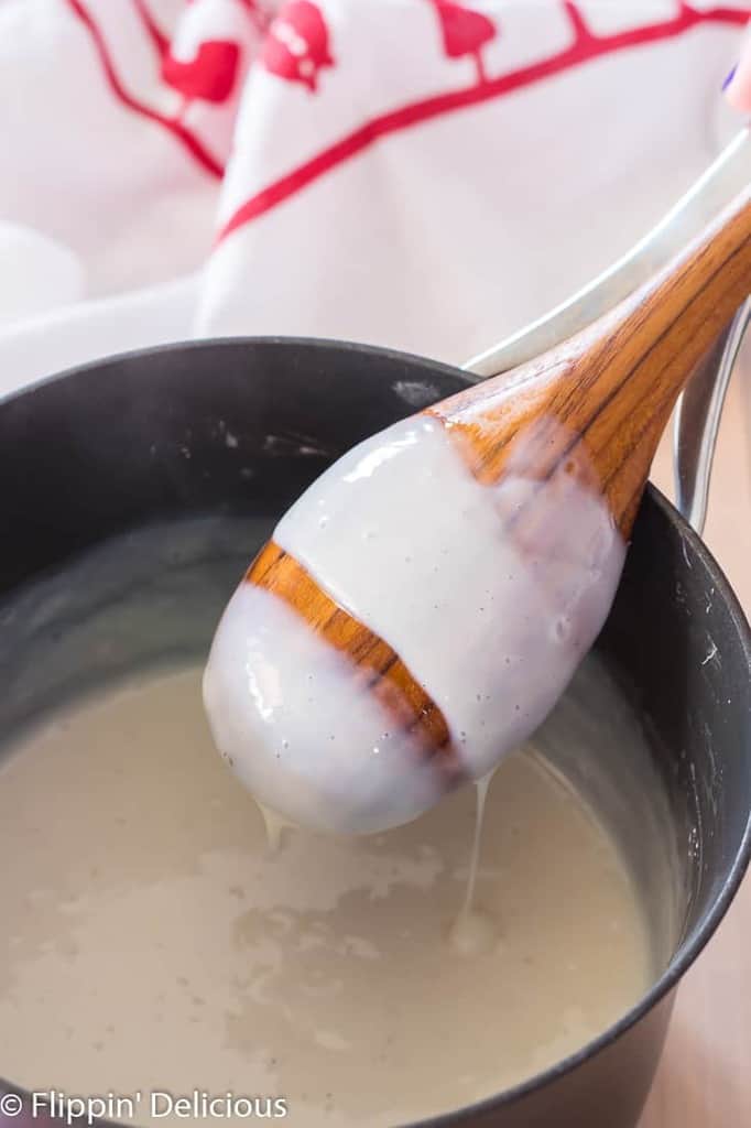 gluten free pudding coating the back of a wooden spoon over a saucepan with dish towel in the back 