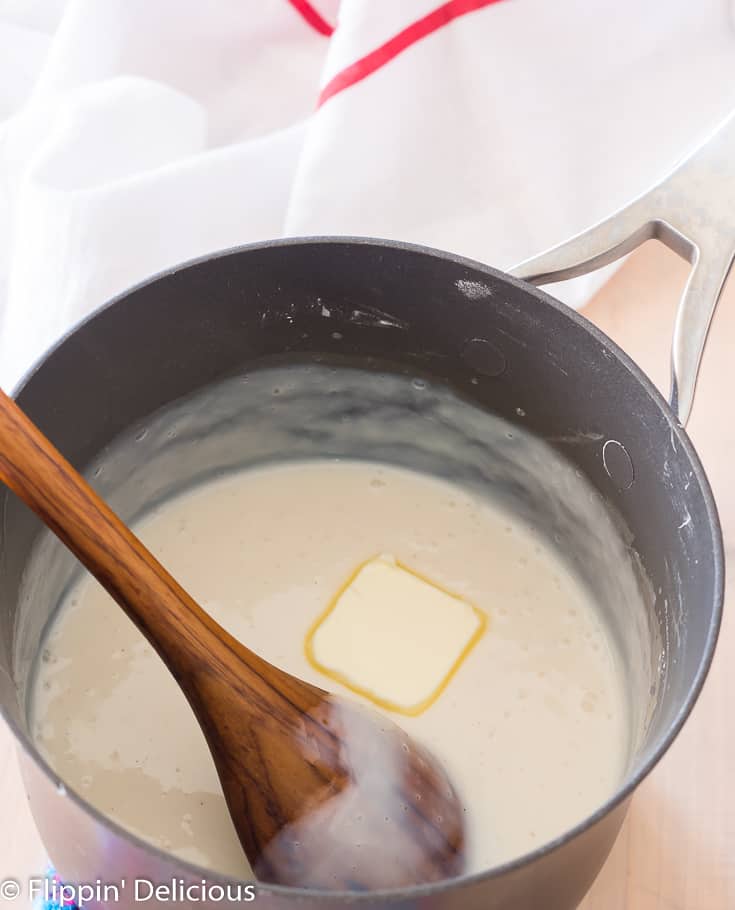 adding butter to gluten free pudding in saucepan with wooden spoon 