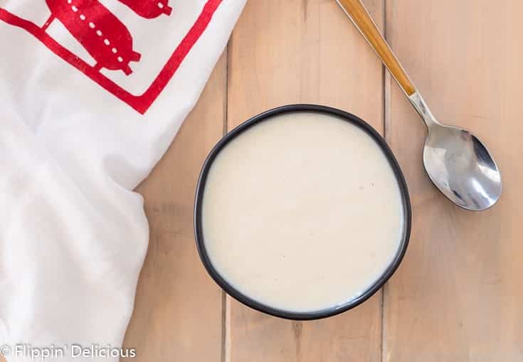 overhead gluten free pudding in black bowl with spoon and red and white dish towel on wooden table