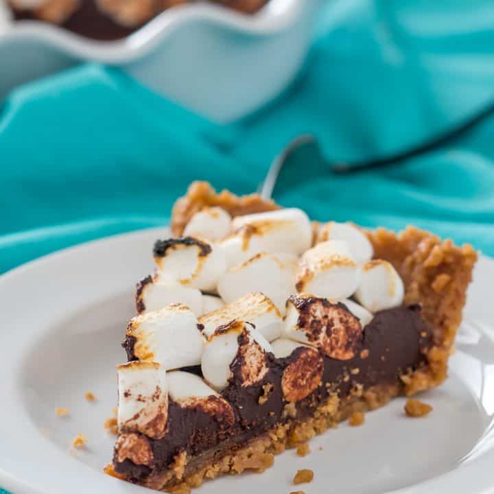 slice of vegan gluten free s'mores fudge pie with toasted marshmallows on a white plate with a teal dish towel and full pie in the background