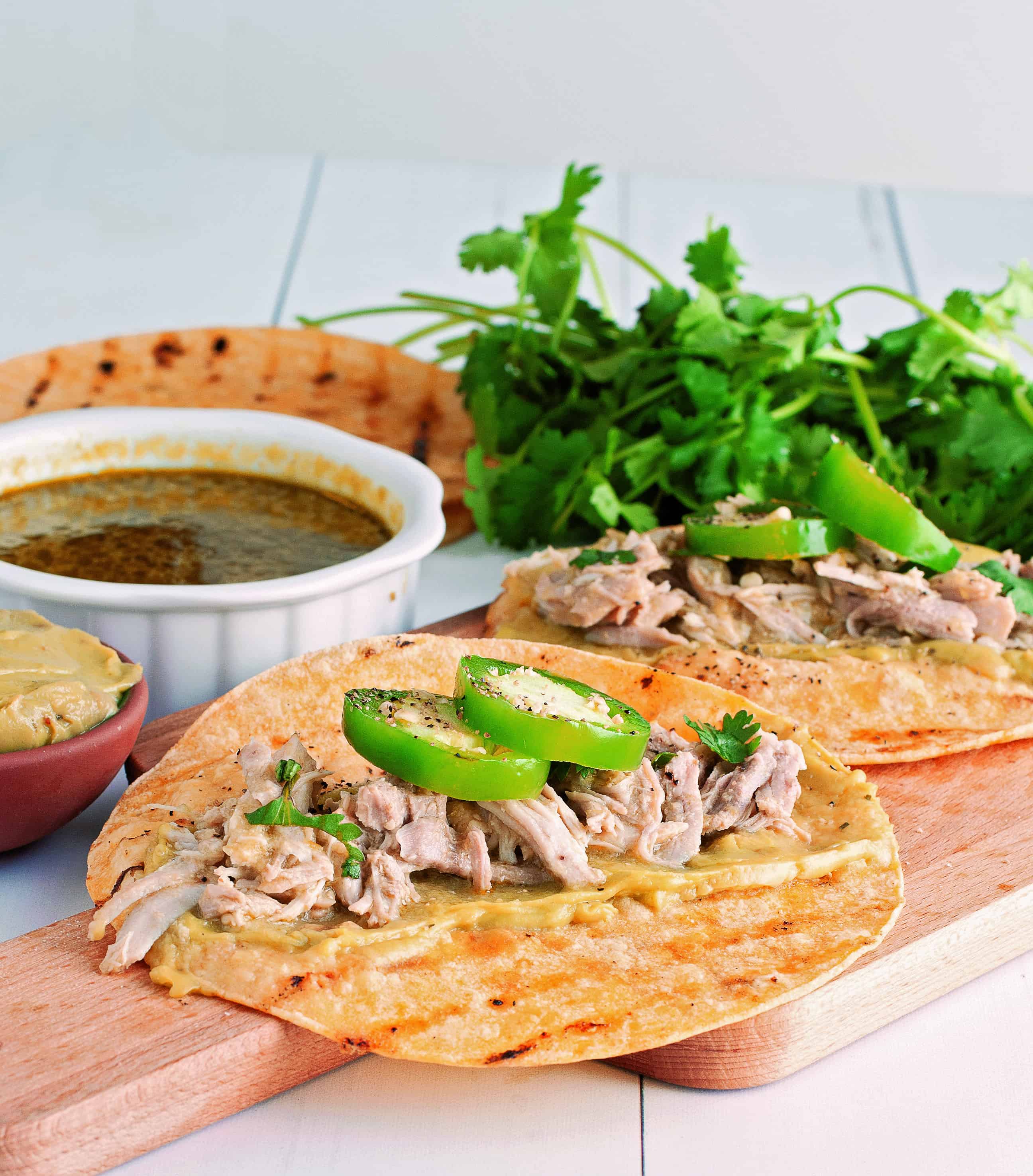 instant pot tomatillo pork tacos on a wooden cutting board with dipping sauce and cilantro in the background
