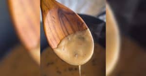 how image of gluten free cream of mushroom soup falling off of wooden spoon into pan of gluten free mushroom soup