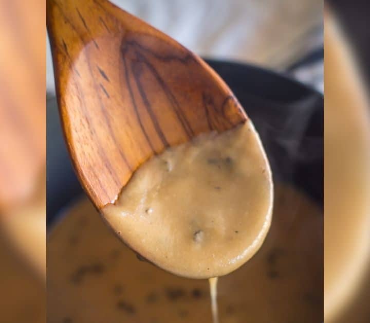 how image of gluten free cream of mushroom soup falling off of wooden spoon into pan of gluten free mushroom soup