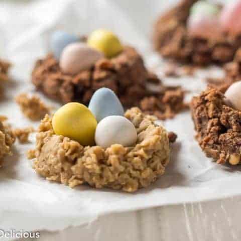 sunflower seed butter and chocolate no bake oatmeal cookie birds nest with chocolate eggs and jelly beans on a piece of parchment paper on a grey table