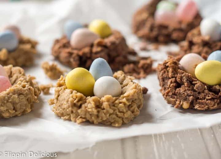 sunflower seed butter and chocolate no bake oatmeal cookie birds nest with chocolate eggs and jelly beans on a piece of parchment paper on a grey table