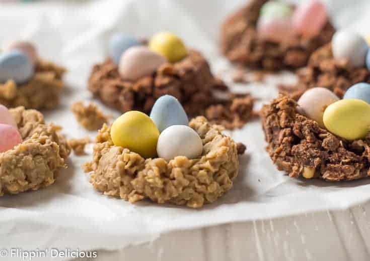 sunflower seed butter and chocolate no bake oatmeal cookie birds nest with chocolate eggs and jelly beans on a piece of parchment paper on a grey table