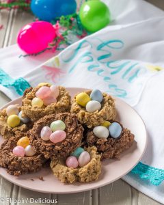 gluten free birds nest cookies on a pink plate on a gray table with a spring tea towel and bright green pink and blue plastic easter eggs