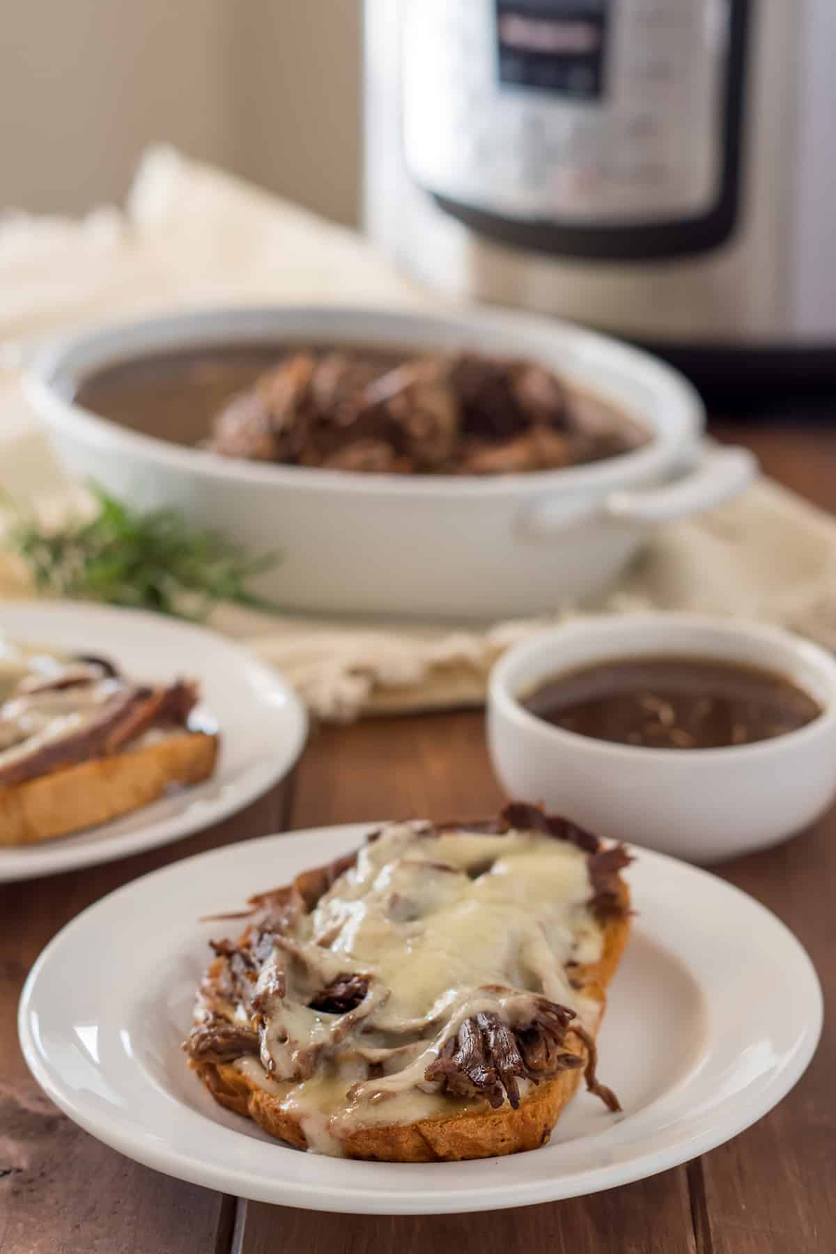 open face gluten free french dip sandwich on a white plate with a small white dish of au jus and another sandwich in the background