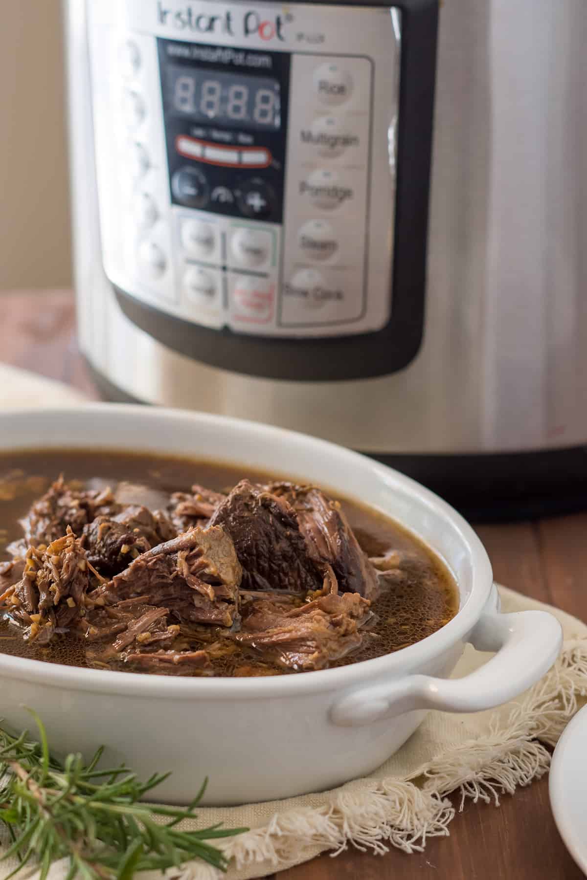 oval dish filled with instant pot gluten free french dip braised beef in front of an instant pot