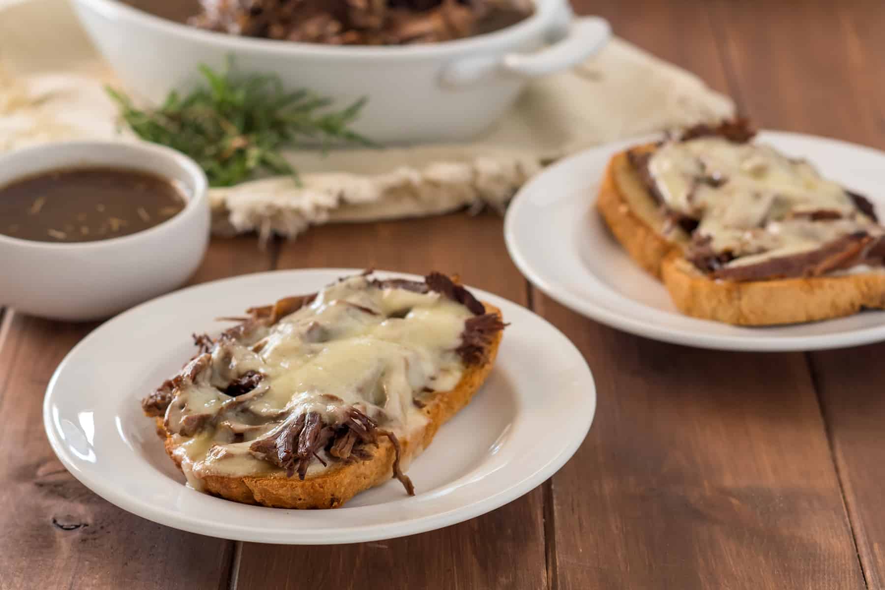 open face gluten free french dip sandwich on a white plate with a small white dish of au jus and another sandwich in the background