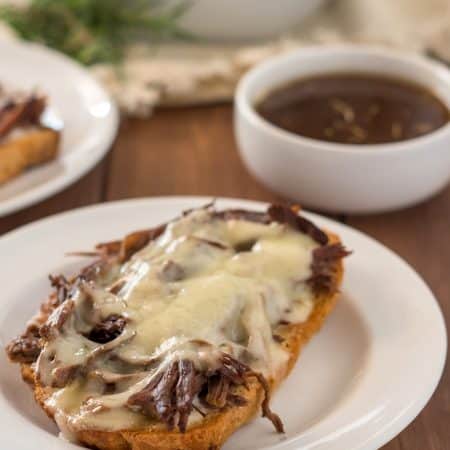 open face gluten free french dip sandwich on a white plate with a small white dish of au jus and another sandwich in the background