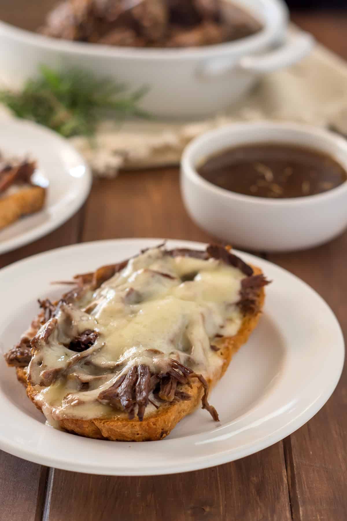 open face gluten free french dip sandwich on a white plate with a small white dish of au jus and another sandwich in the background