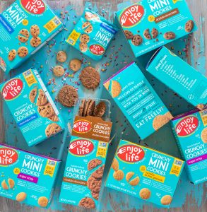 overhead of enjoy life crunchy cookies and mini cookies in packaging on a teal table, with sprinkles spilled all over