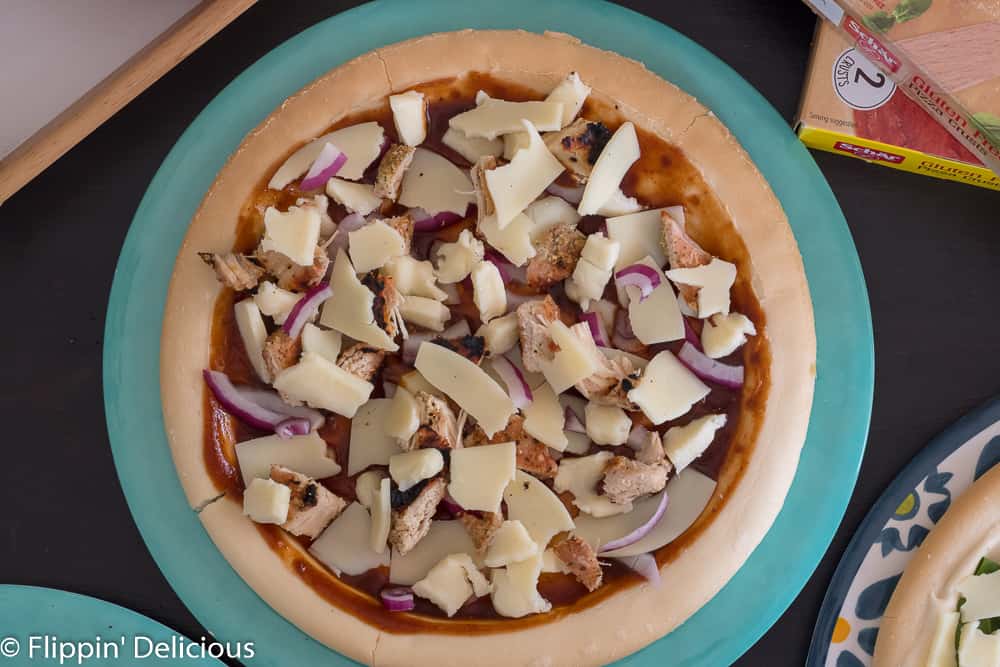 overhead of gluten free pizza topped with barbecue sauce, griled chicken and red onion