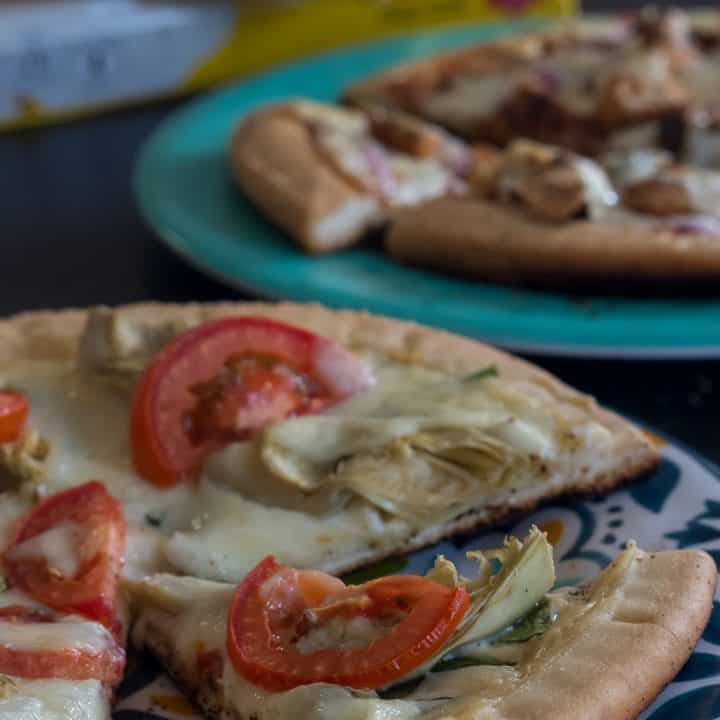 gluten free pizza topped with tomatoes spinach and artichokes on a blue plate