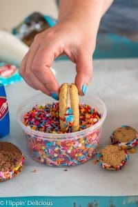 hand holding gluten free sandwich cookie, rolling exposed filled center in sprinkles