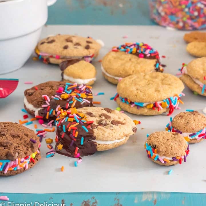 gluten free sandwich cookies dipped in chocolate with sprinkleson a piece of parchment paper on a teal table