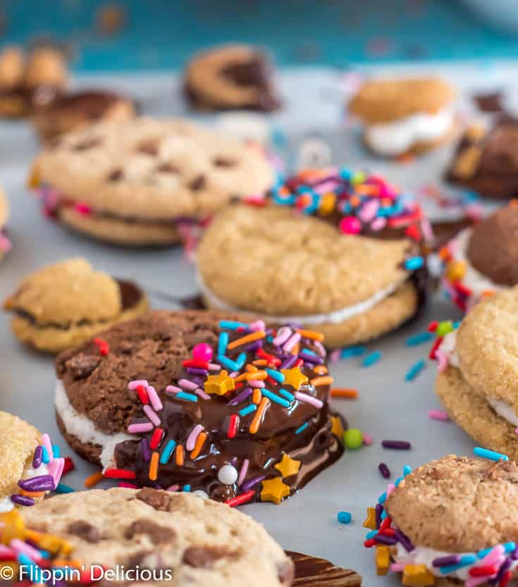 gluten free chocolate sandwich cookie half dipped in chocolate and sprinkles, on a a piece of parchment paper surrounded by more dipped and sprinkled gluten free sandwich cookies