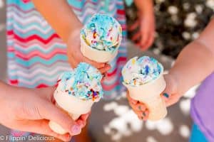 three girls holding gluten free ice cream cones, each with a scoop of no churn vegan cake batter ice cream with blue frosting and sprinkles swirled in